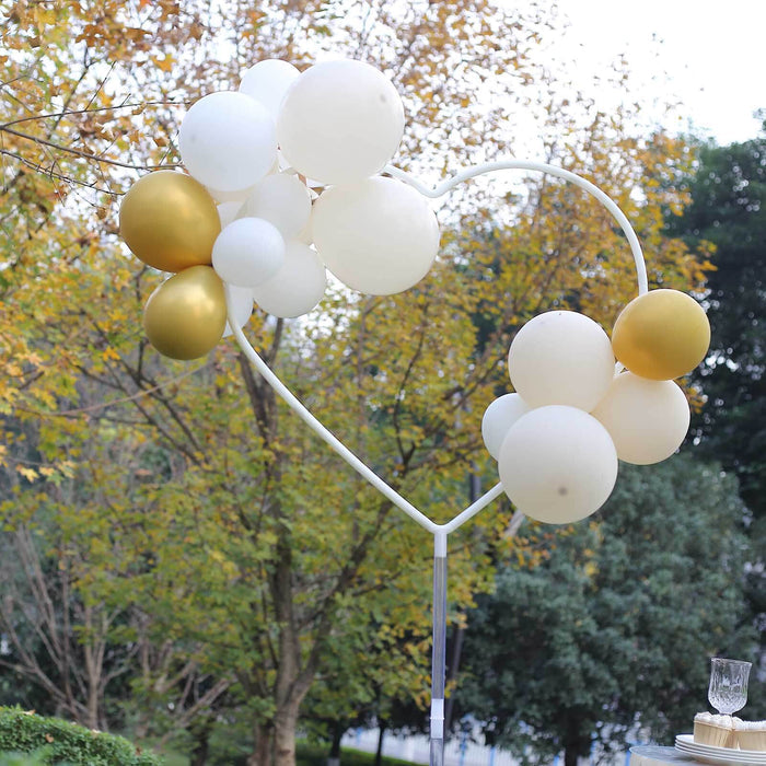 Heart-shaped balloon arch with gold and white balloons in an outdoor setting.