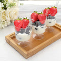 Yogurt parfaits with strawberries and blueberries in clear cups on a wooden tray.