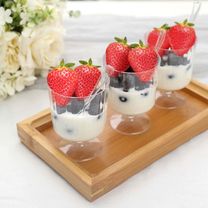 Yogurt parfaits with strawberries and blueberries in clear cups on a wooden tray.