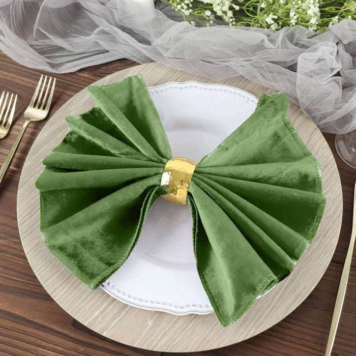 Green velvet napkin tied with a gold ring on a white plate.