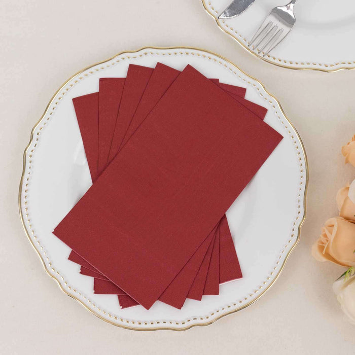 Set of burgundy napkins on a decorative white plate with a gold rim.
