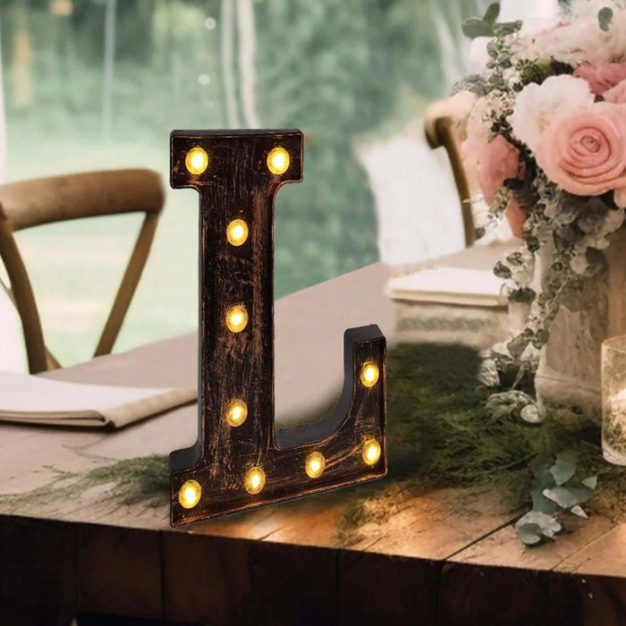 Rustic marquee letter "L" with lights on a table in a decorated setting.