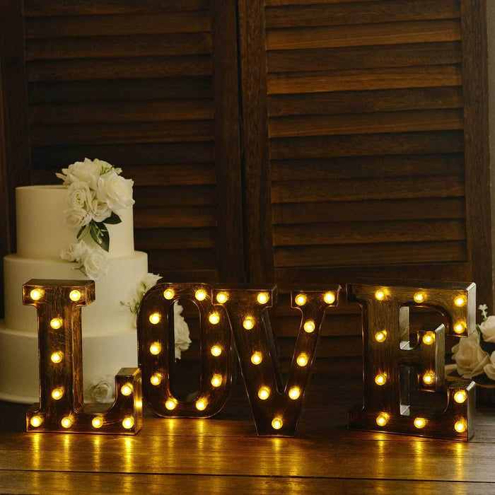 Decorative marquee letters spelling "LOVE" with warm lights, styled with wedding cake.
