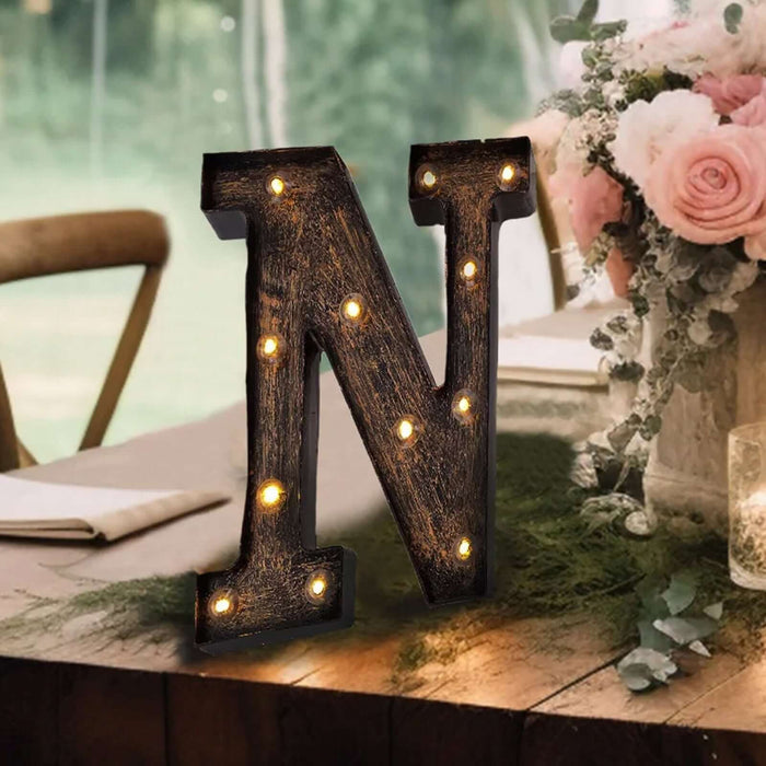 Decorative light-up letter "N" on a rustic table with flowers and greenery.