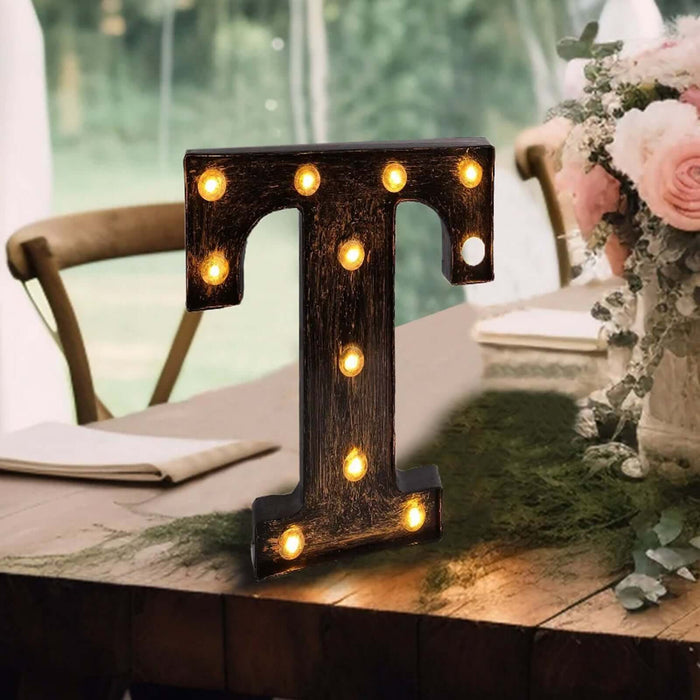 Decorative light-up letter "T" on a table with flowers and greenery.