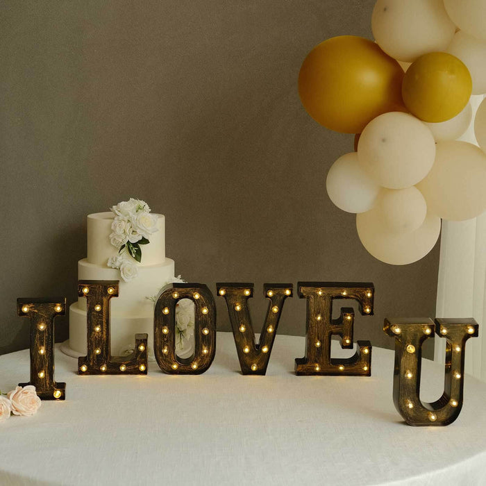 Illuminated "I LOVE U" marquee letters with balloons and a cake in a festive setting.