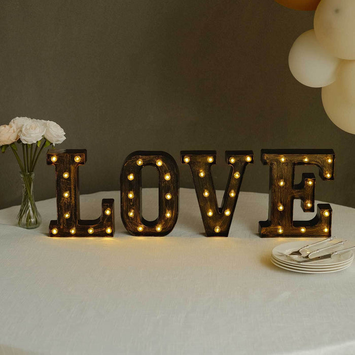 Decorative illuminated "LOVE" letters on a table with flowers and plates.