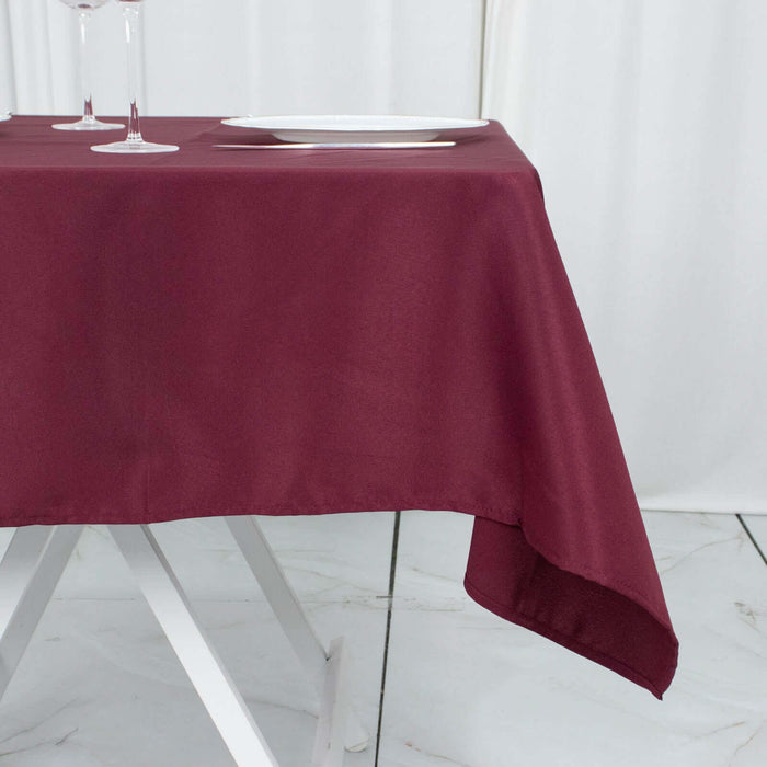 Burgundy tablecloth draped over a table with plates and glasses.