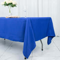 Blue tablecloth draped over a table with a glass and flowers in the background.