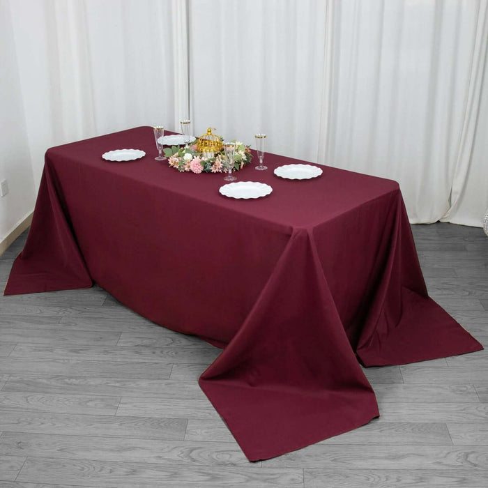 Burgundy tablecloth draped on a dining table with decorative plates and flowers.