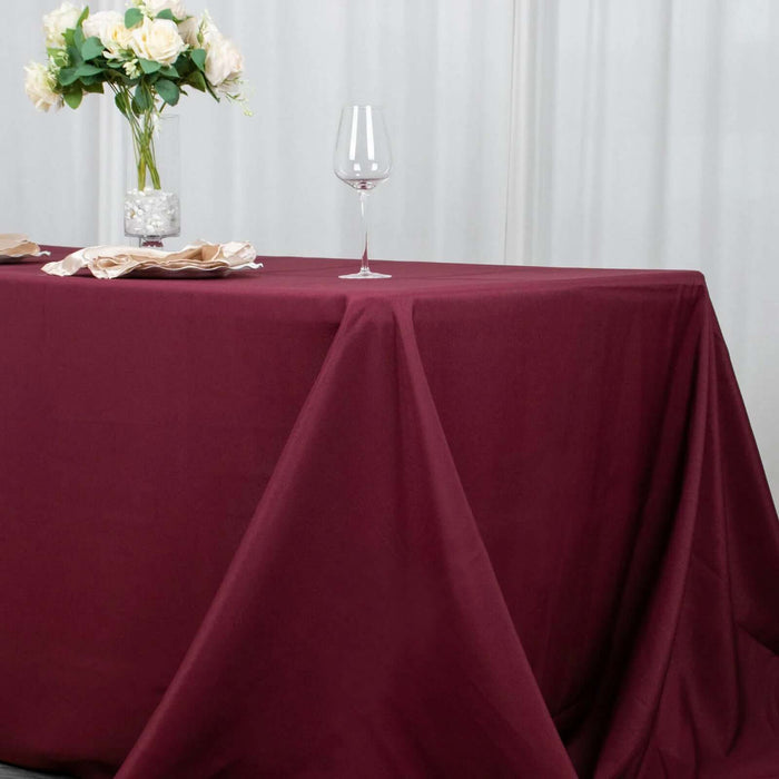 Burgundy tablecloth draped elegantly on a table with vase and glass.
