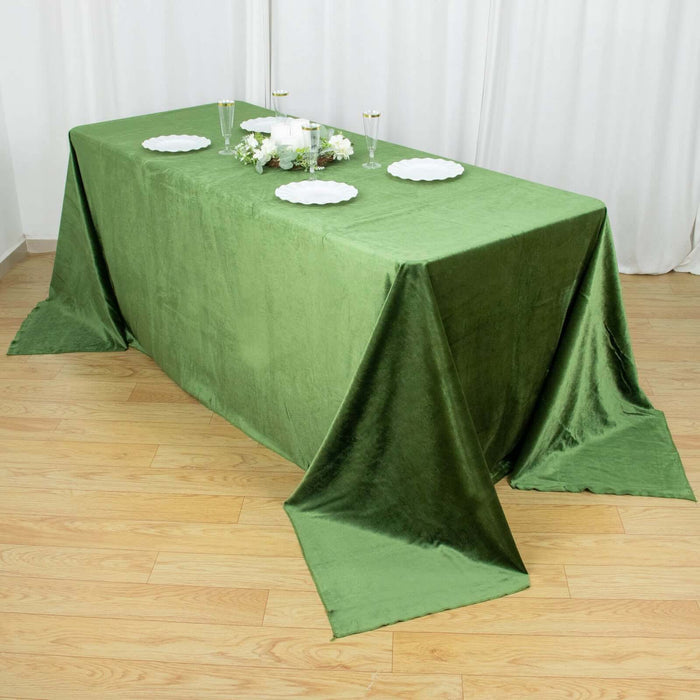 Green velvet tablecloth on a wooden table with decorative plates and flowers.