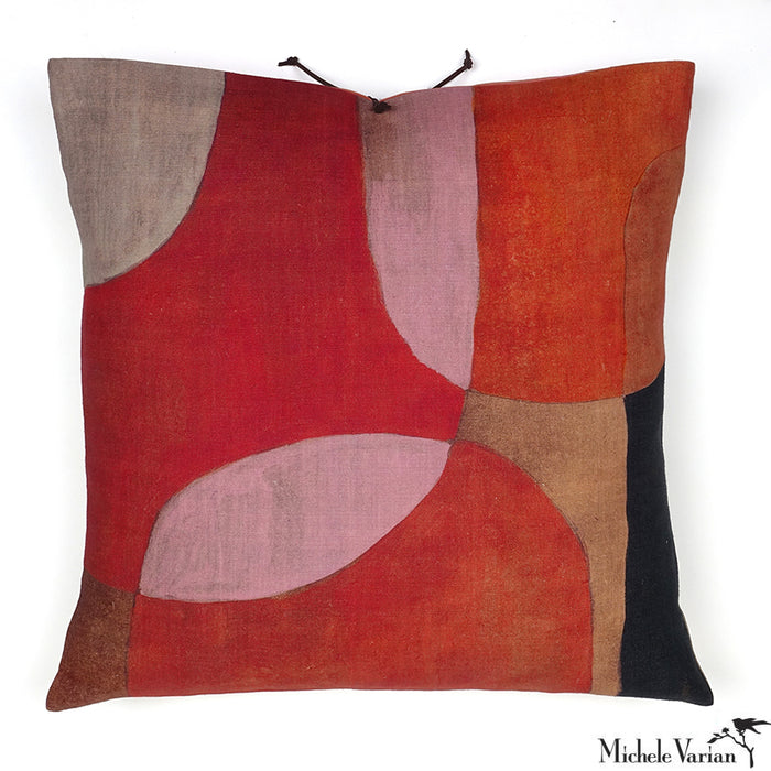 A square-shaped linen throw pillow with an abstract geometric pattern in red, black, gray, and pink, featuring a leather tie closure. Designed by Michele Varian and made in New York.