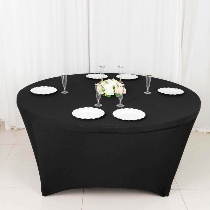 Black round table with white plates and floral centerpiece, set for dining.