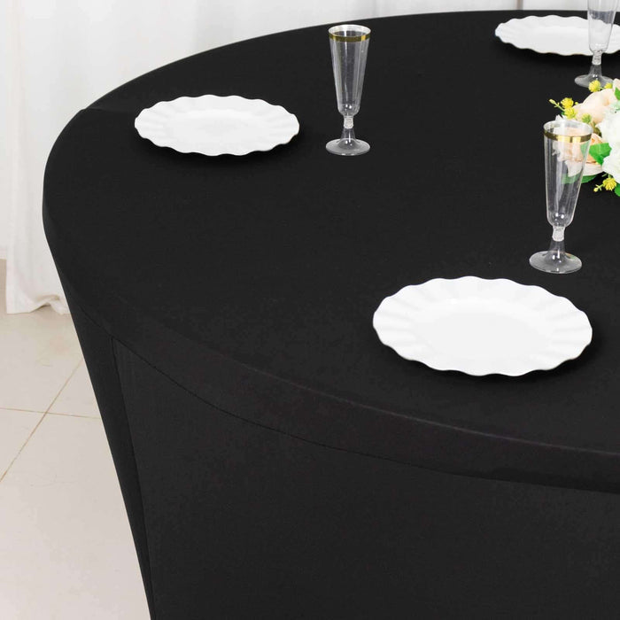 Black round table with white plates and elegant glassware set for dining.